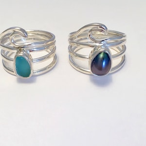 May include: Two silver rings with wave designs. One ring features a teal gemstone, while the other has a black pearl.