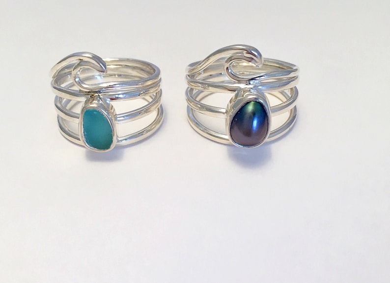 May include: Two silver rings with wave designs. One ring features a teal gemstone, while the other has a black pearl.
