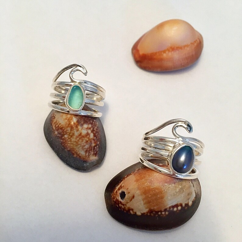 May include: Two silver rings with a wave design. One ring has a light blue stone and the other has a dark blue stone.
