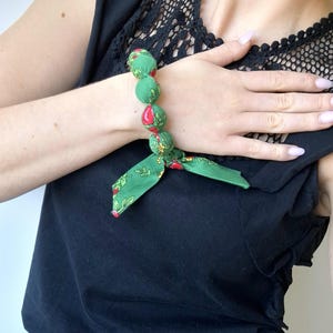 May include: A green fabric bracelet with red and yellow floral print. The bracelet is made of fabric balls and has a bow tie closure.