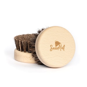 Op de afbeelding: Twee borstels met houten handvatten en natuurlijke borstels. De borstel rechts heeft het logo "SaunHat" gegraveerd op het handvat.
