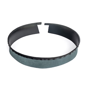 May include: A black leather ring with a grey fabric lining. The ring is open on one side and has a stitched edge.
