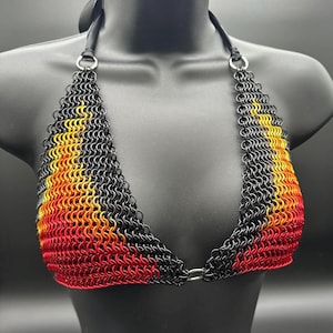 May include: A chainmail bikini top in black, red, yellow, and orange. The halter top features a gradient color scheme, transitioning from red at the bottom to yellow and black at the top. The top is displayed on a black mannequin.