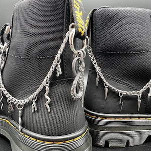 May include: Black canvas boots with silver chains and charms. The chains have various charms, including a snake, lightning bolts, and spikes.