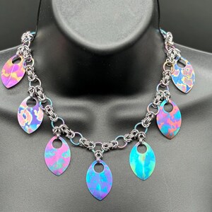 May include: A silver chain necklace with multiple iridescent blue, pink, and purple leaf-shaped pendants.