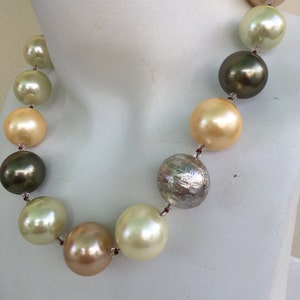 May include: A necklace made of large, round, cream, gold, and green beads. The beads are strung on a thin, brown cord. The necklace is displayed on a white mannequin.