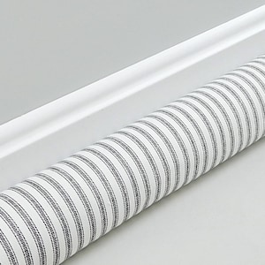 May include: A cylindrical roll of fabric featuring a repeating pattern of thin, dark charcoal gray vertical stripes set against a crisp white background. The stripes are composed of fine, textured lines that run parallel along the length of the roll.