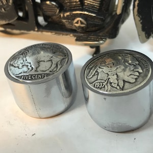 Könnte beinhalten: Zwei silberne Motorradlenker-Endkappen mit einem Büffel-Nickel und einem Indianer-Nickel, die oben eingelassen sind. Der Büffel-Nickel sagt "FIVE CENTS" und der Indianer-Nickel sagt "LIBERTY" und "1937".