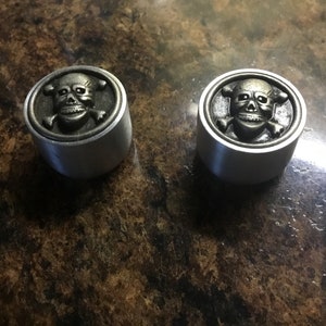 May include: Two silver skull and crossbones knobs. The knobs are round and have a raised skull and crossbones design.