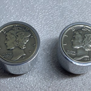 Könnte beinhalten: Zwei silberfarbene Metallknöpfe mit einer silberfarbenen Münze, die oben eingelassen ist. Die Münzen sind beide US-Mercury-Dimes, eine aus dem Jahr 1916 und die andere aus dem Jahr 1942.