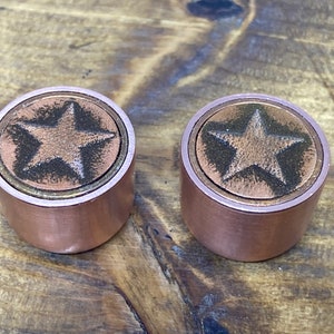 Peut inclure: Deux boutons de couleur cuivre avec un motif d'étoile. Les boutons sont ronds et ont un bord surélevé autour de l'étoile.