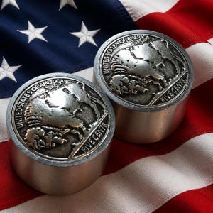 May include: Two cylindrical metal paperweights featuring a raised relief design of the United States Buffalo nickel on the top surface. Each piece displays the text United States of America and Five Cents surrounding the iconic bison image.