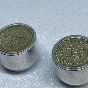 May include: Two silver bottle stoppers with a gold-colored top featuring an eagle design surrounded by stars.