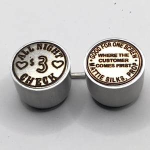 May include: Two silver-colored metal objects connected by a thin bar. One has the text "ALL NIGHT $3 CHECK" and two heart symbols. The other reads "GOOD FOR ONE SCREW WHERE THE CUSTOMER COMES FIRST MATTIE SILKS, PROP."