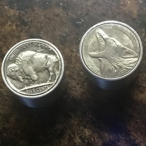 以下が含まれることがあります： 銀色のコインが2つ。1つはバッファローと「United States of America」と「Five Cents」の文字が刻まれている。もう1つは、うなり声をあげているオオカミが刻まれている。