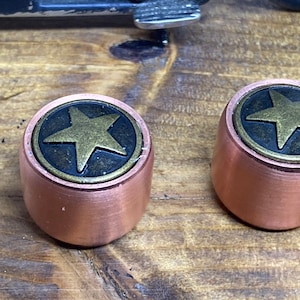 May include: Two copper-colored knobs with a star-shaped design. The stars are gold-colored and have a black background.