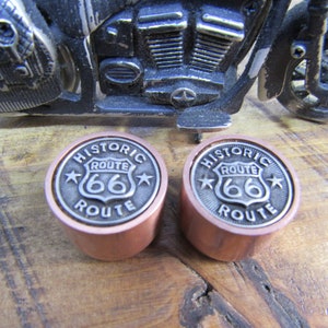 Könnte beinhalten: Zwei kupferne Motorrad-Ventilkappen mit einem silbernen Metalldesign mit dem Text "Historic Route 66" und einem Stern auf jeder Seite.