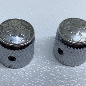 May include: Two silver guitar knobs with a 1944 US Liberty Head nickel design on the top. The knobs have a diamond-shaped pattern on the sides.