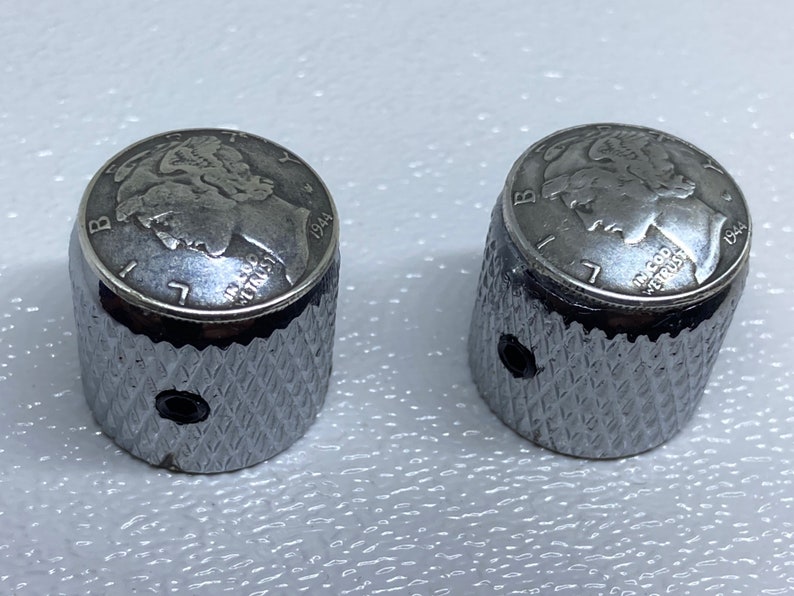 May include: Two silver guitar knobs with a 1944 US Liberty Head nickel design on the top. The knobs have a diamond-shaped pattern on the sides.
