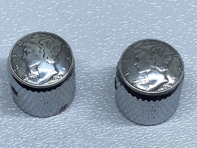 May include: Two silver-colored guitar knobs with a 1944 Mercury dime design on the top. The knobs have a diamond-shaped pattern on the sides.