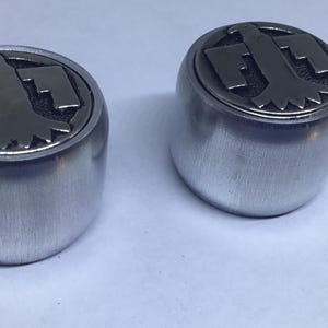 Op de afbeelding: Twee zilveren metalen knoppen met een gestileerd adelaarontwerp aan de bovenkant. De adelaar bevindt zich in een cirkelvormig ontwerp met een donkergrijze afwerking.