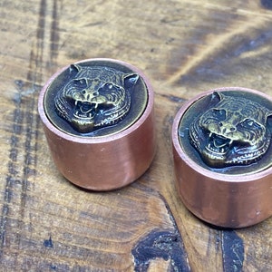 May include: Two copper bottle stoppers with a tiger head design. The tiger heads are made of brass and have a detailed, realistic design.