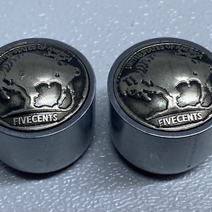 May include: Two silver-colored metal bottle caps with a raised design of a buffalo and the words "United States of America" and "Five Cents".