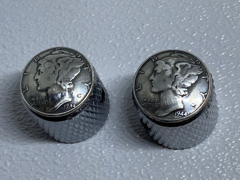 May include: Two silver-toned guitar tuning knobs with a 1944 Walking Liberty Half Dollar coin design. The knobs have a knurled, textured surface.