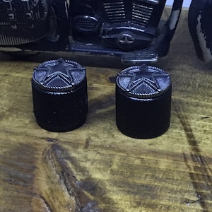 May include: Two black metal knobs with a silver star design on the top. The knobs are on a wooden surface.