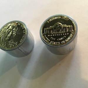 May include: Two gold-coloured US coins, one a penny with the profile of Abraham Lincoln and the words "In God We Trust" and "Liberty 2016", and the other a nickel with the image of the Jefferson Memorial and the words "E Pluribus Unum", "United States of America", "Five Cents", and "Monticello".