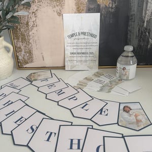 May include: A collection of religious event supplies, including a banner spelling "TEMPLE PRIESTHOOD", a flyer with event details, and a water bottle with a religious image. The banner has navy blue lettering on white pennants.