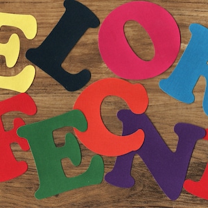 May include: Colourful felt letters spelling out the word "ELORECNI" on a wooden background.