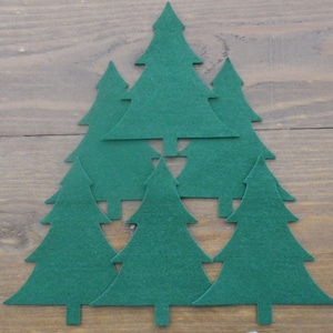 May include: Seven green felt Christmas tree cutouts arranged in a pyramid shape on a woodgrain surface.