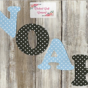 May include: A set of felt letters spelling out the name "NOAH". The letters are in black and white polka dot patterns. The letters are on a light wood background. The letters are for a craft project.