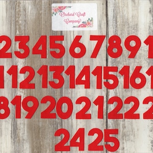 May include: Red felt numbers from 1 to 25 on a woodgrain background. The numbers are in a bold, blocky font. The text "Orchard Craft Company" is visible in the top right corner.