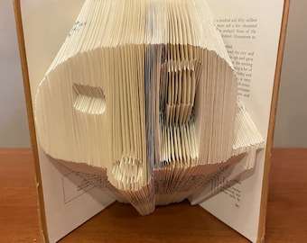 May include: A book folded into the shape of a peace sign. The book is open and the pages are folded to create the shape. The book is made of white paper and has a brown cover.