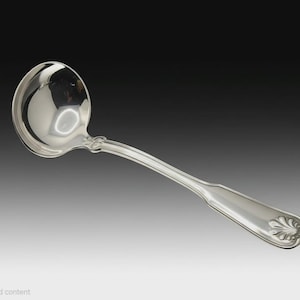 May include: A polished silver-toned soup ladle featuring a deep, rounded bowl and a curved handle. The handle is decorated with a subtle shell-like motif at the base and a smooth, tapered design that extends toward the bowl.