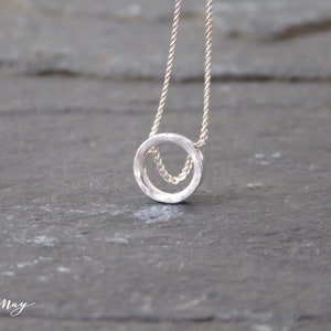 A tiny, hammered circle made of real silver hangs on a delicate sterling silver chain displayed on a black surface.