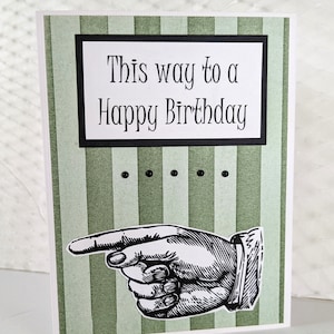 May include: Green and white striped card with a black border around the text "This way to a Happy Birthday". A black and white illustration of a pointing hand is below the text.