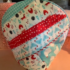 May include: A round, quilted, fabric cover with a patchwork design featuring red, white, and blue colors. The cover has a variety of patterns, including polka dots, gingham, and a floral print. The cover is decorated with a white lace trim and a white braided trim.