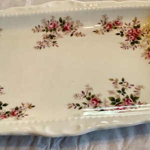 May include: A white rectangular serving tray with a gold trim and a floral design featuring pink roses and green leaves.