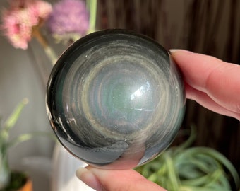 May include: A black obsidian sphere with iridescent swirls and a green center. The sphere is smooth and polished.