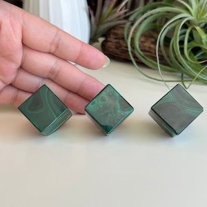 May include: Three green malachite gemstone cubes with a swirling pattern. The cubes are smooth and polished.