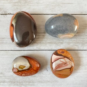 May include: Four smooth, polished stones with unique patterns and colors. The stones are brown, gray, and white with swirls and bands of color.