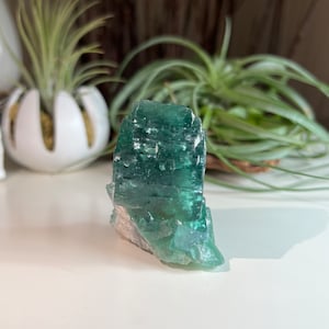 May include: A green fluorite crystal with a layered, striated texture. The crystal is a natural, raw specimen with a translucent, glassy appearance.