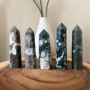 May include: Five green and white agate crystal points, also known as moss agate, arranged in a row on a wooden surface.