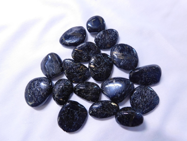 May include: A collection of smooth, dark blue and black tumbled stones with a shimmery, iridescent finish. The stones are oval-shaped and have a natural, polished look.
