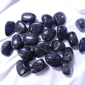 May include: A collection of black tumbled stones with a shimmery, iridescent finish. The stones are smooth and polished, and they have a variety of shapes and sizes.