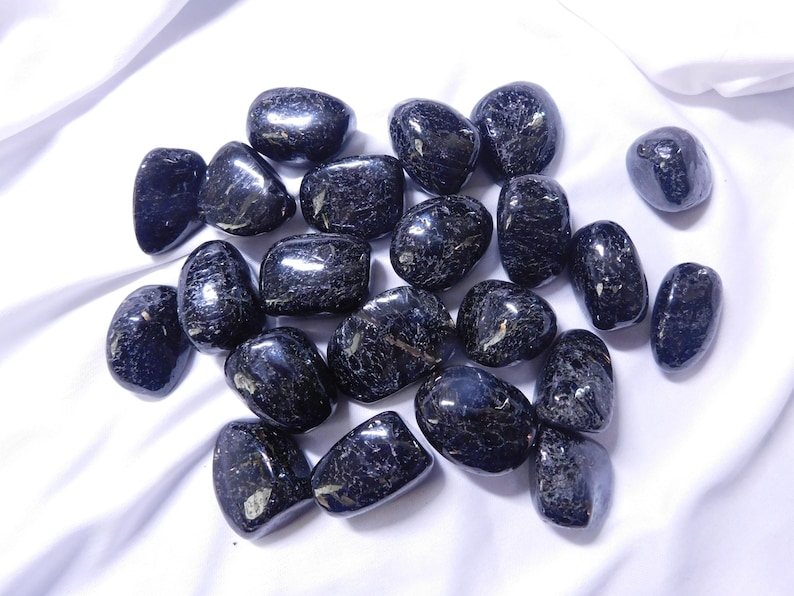 May include: A collection of black tumbled stones with a shimmery, iridescent finish. The stones are smooth and polished, and they have a variety of shapes and sizes.