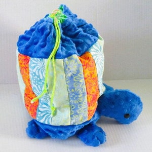 May include: A blue and orange patchwork drawstring bag shaped like a turtle. The bag is made of soft fabric and has a green drawstring.